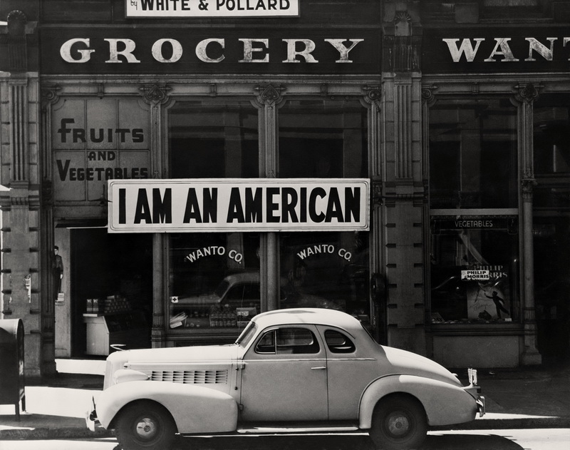 Dorothea Lange.  Oakland, California, marzo 1942. Un grande cartello con la scritta “SONO AMERICANO” sulla vetrina di un negozio l'8 dicembre, il giorno dopo Pearl Harbor. Il negozio era stato chiuso in seguito all'ordine impartito alle persone di origine giapponese di evacuare alcune zone della costa occidentale. Il proprietario, laureato all'Università della California, sarà ospitato insieme a centinaia di sfollati nei centri della War Relocation Authority per tutta la durata della guerra.  The New York Public Library | Library of Congress Prints and Photographs Division Washington